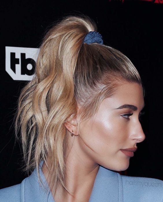 Hailey Bieber wearing a top ponytail with a blue scrunchie and wavy hair looks cool and cute