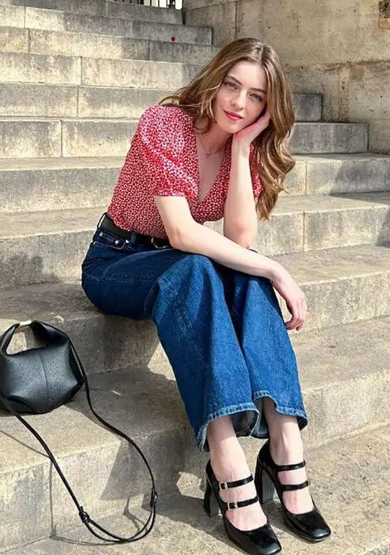 a Parisian chic outfit with a pink printed blouse, blue jeans, black Mary Jane shoes and a small black bag is cool