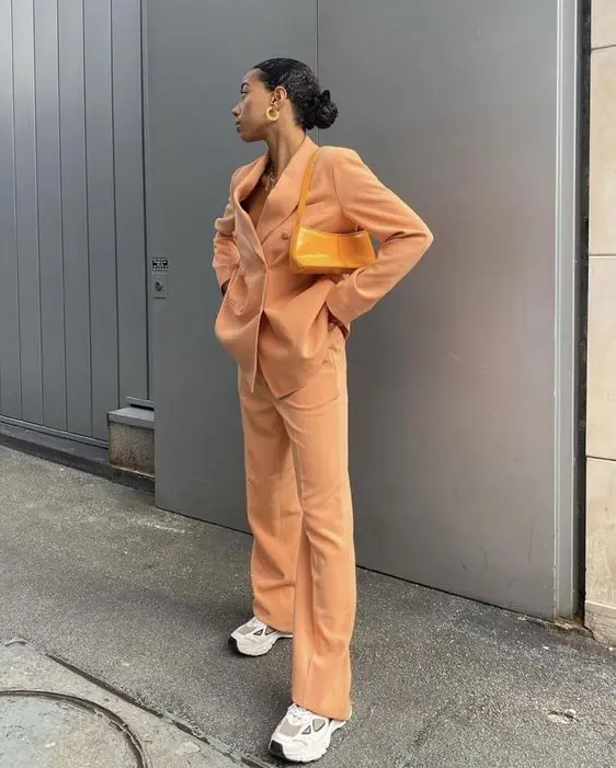 a Peach Fuzz pantsuit with an oversized blazer, a yellow bag and trainers are a super trendy sporty outfit