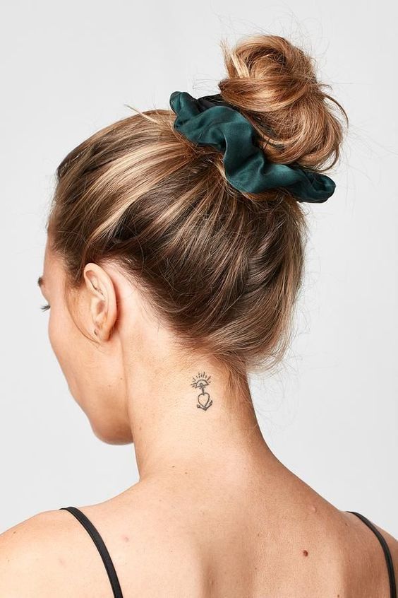 a ballerina top knot with a volumetric top and a dark green silk scrunchie are a lovely and simple hairstyle