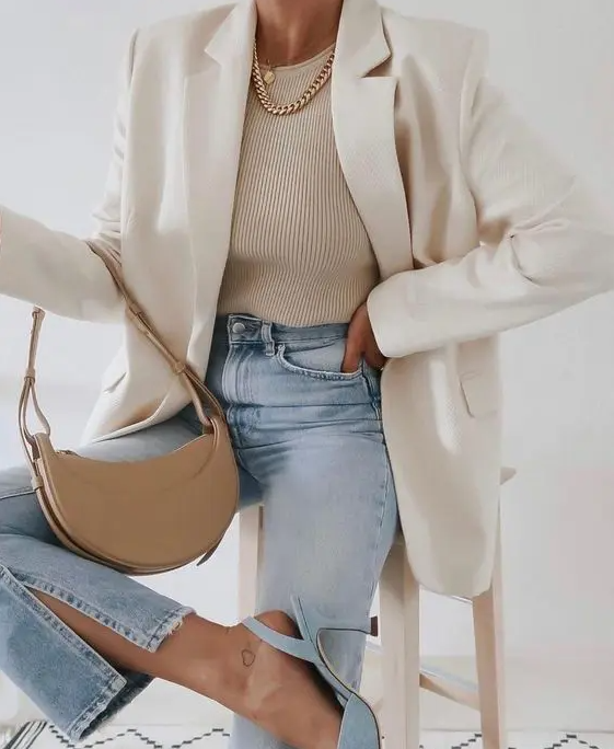 a beautiful spring outfit with a neutral top, bleached jeans, blue heels, layered necklaces, a white blazer and a tan baguette bag