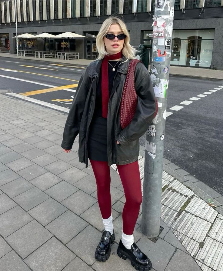 a bold look with a black top and mini skirt, a black leather jacket, black chunky loafers, cherry red tights, a scarf and a bag and white sorkcs