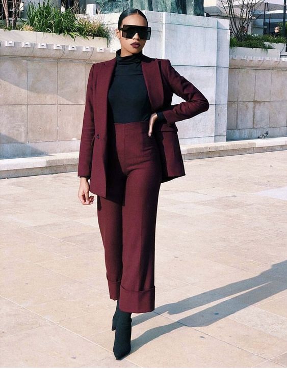 a bold minimalist look with a burgundy pantsuit with cropped pants, black sock boots, a black turtleneck and futuristic sunglasses
