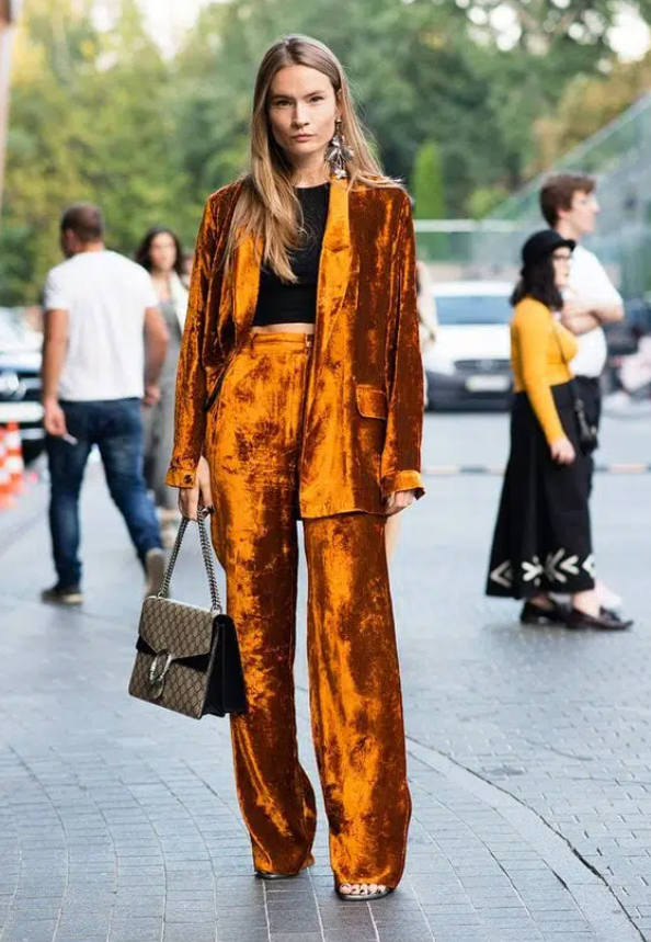 a bold orange crushed velvet pantsuit, a black crop top, metallic shoes, a bag and statement earrings