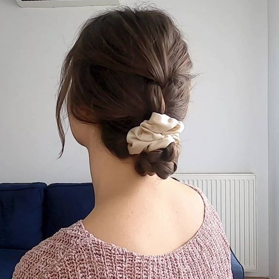 a braided ending up in a low bun, with a vanilla-colored scrunchie and face-framing hair is a lovely hairstyle