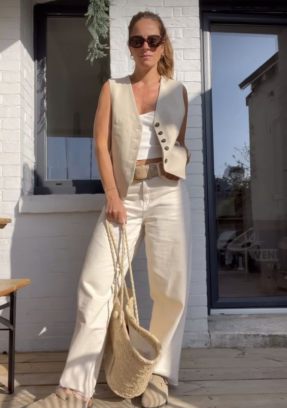 a casual outfit with a white top, a neutral linen waistcoat, white jeans, grey birkenstocks, a woven tote