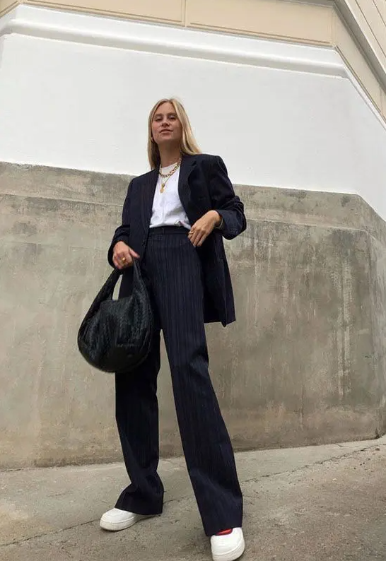 a chic black thin stripe pantsuit, a white t-shirt, layered necklaces, white platform sneakers and a black bag