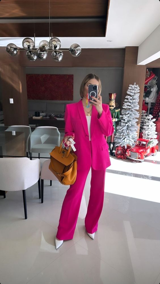 a chic outfit with a fuchsia pantsuit with accented shoulders, a white top, white shoes and an amber leather bag