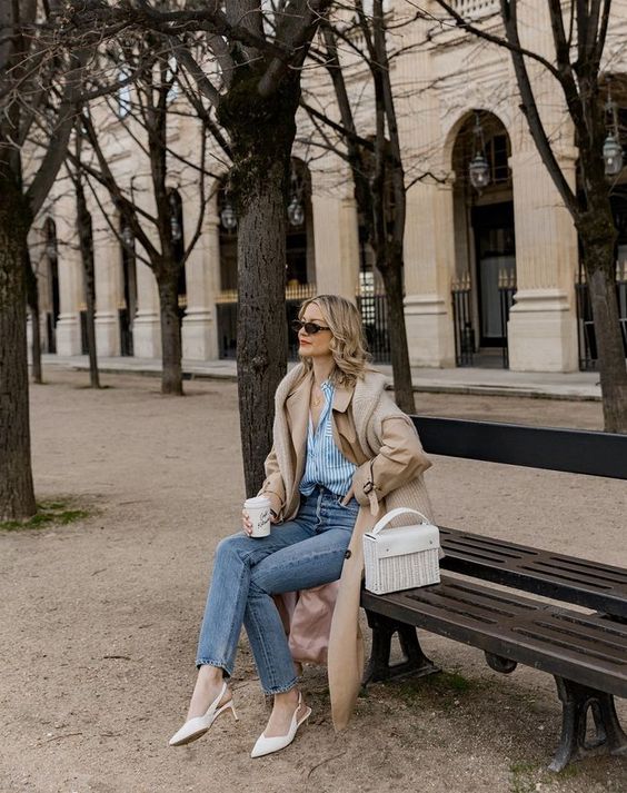 a chic spring look with a blue striped button down, blue jeans, white slingbacks, a tan trench and a white box bag