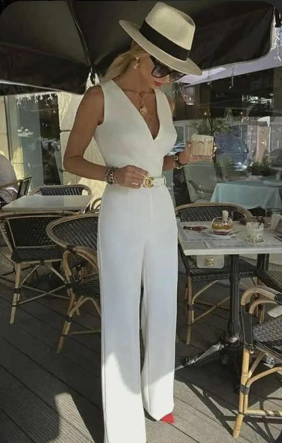 A chic white jumpsuit with wide straps and a V neckline, hot red shoes, jewelry and a hat