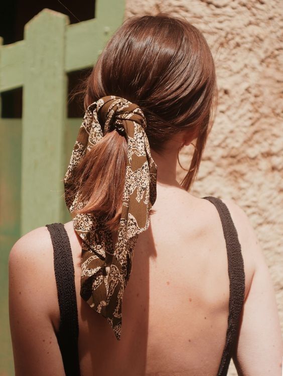A classic low ponytail with a sleek top and face framing hair plus a brown printed scarf as an accessory