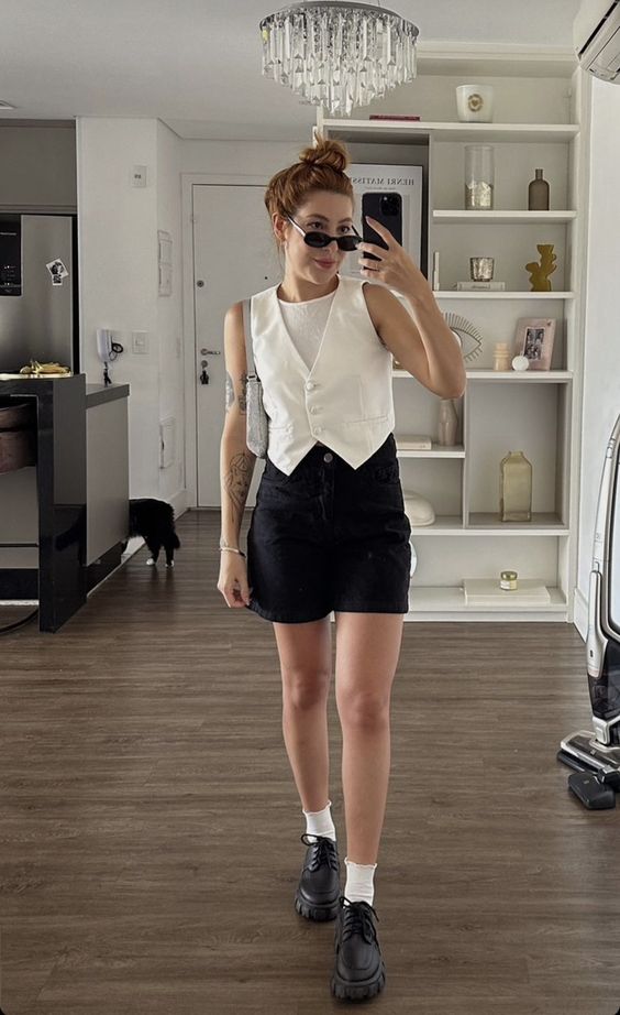 a classy summer outfit with a white top, vest, black shorts, white socks, black chunky shoes and sunglasses