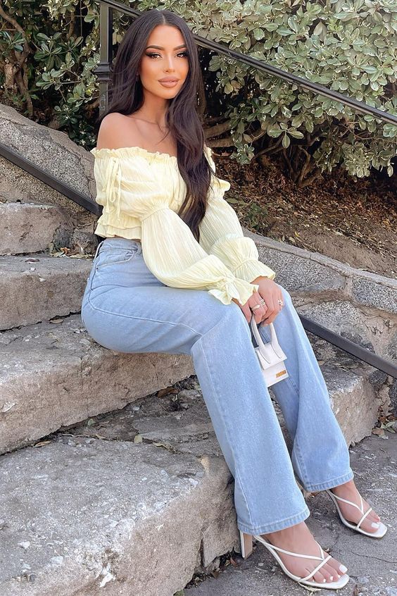 A girlish spring outfit wth a light yellow off the shoulder blouse, blue high waisted jeans, white strappy shoes and a tiny bag