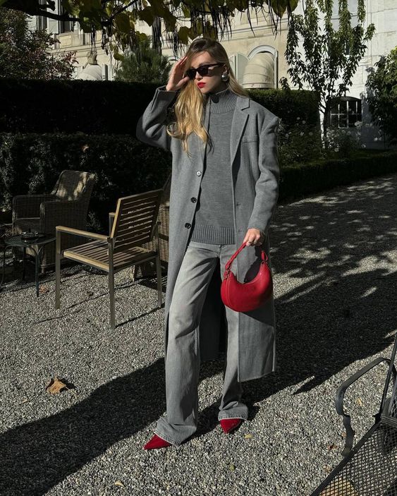 a grey outfit with cherry red accents, an oversized sweater, jeans and a trench plus a red bag and shoes