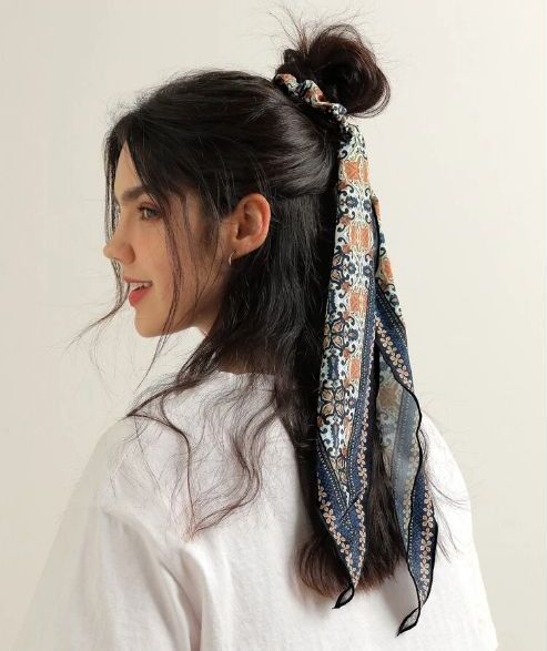 A half updo with a messy top knot, face framing hair and a printed scarf accenting the hairstyle