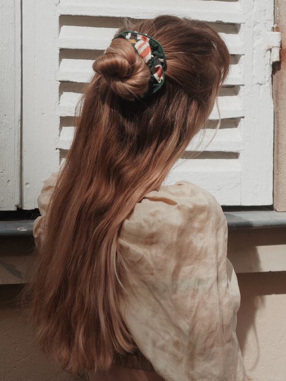 a half updo with a volumetric top, wavy hair down and a bun plus a printed srunchie to make an accent in the hair