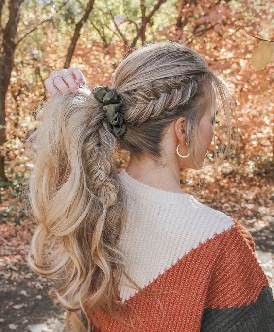 a high ponytail with a side fishtail braid and a volume on top plus face-framing hair and a green scrunchie are a beautiful and a bit boho hairstyle