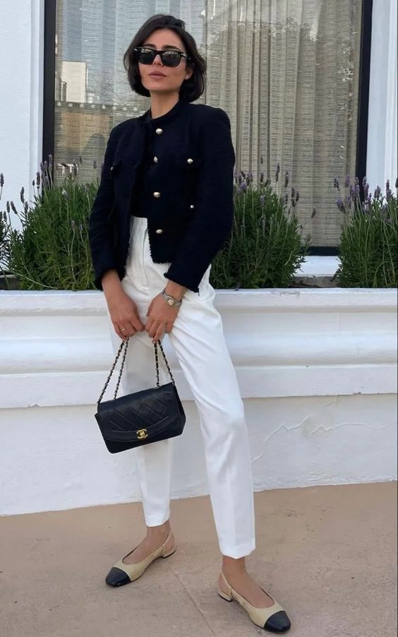 A lovely Old Money outfit wiht a black top, white high waisted pants, two tone shoes, a black cropped blazer and a black bag