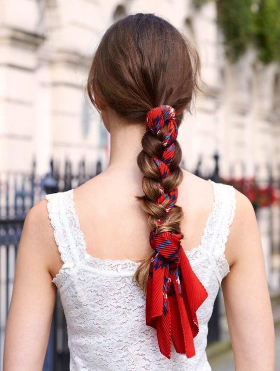 a low braid with a sleek top and a bright red scarf interwoven into the braid are a cool and catchy combo
