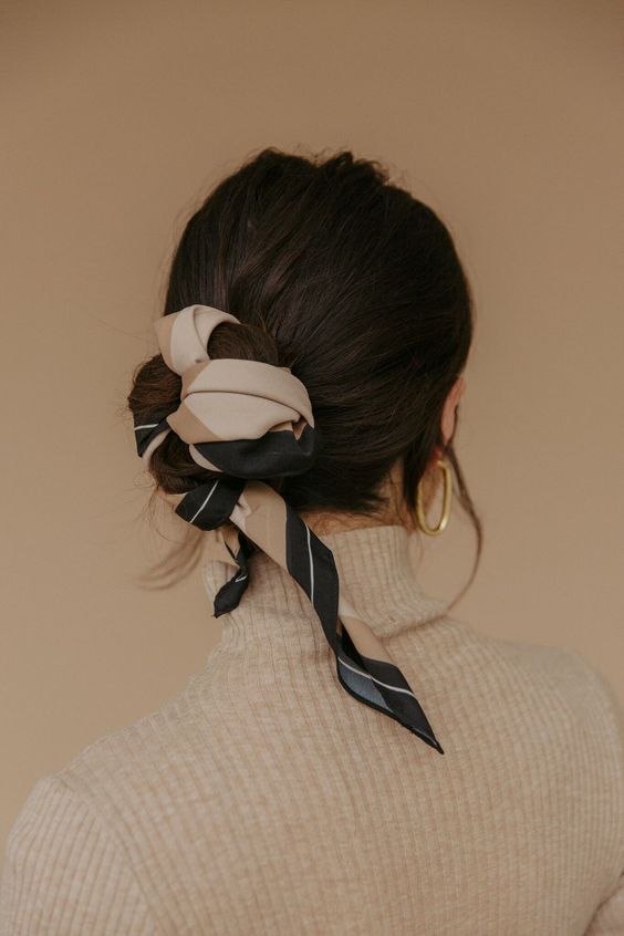 a low bun with a volumetric top and a printed scarf interwoven are a lovely combo for a trendy and chic look