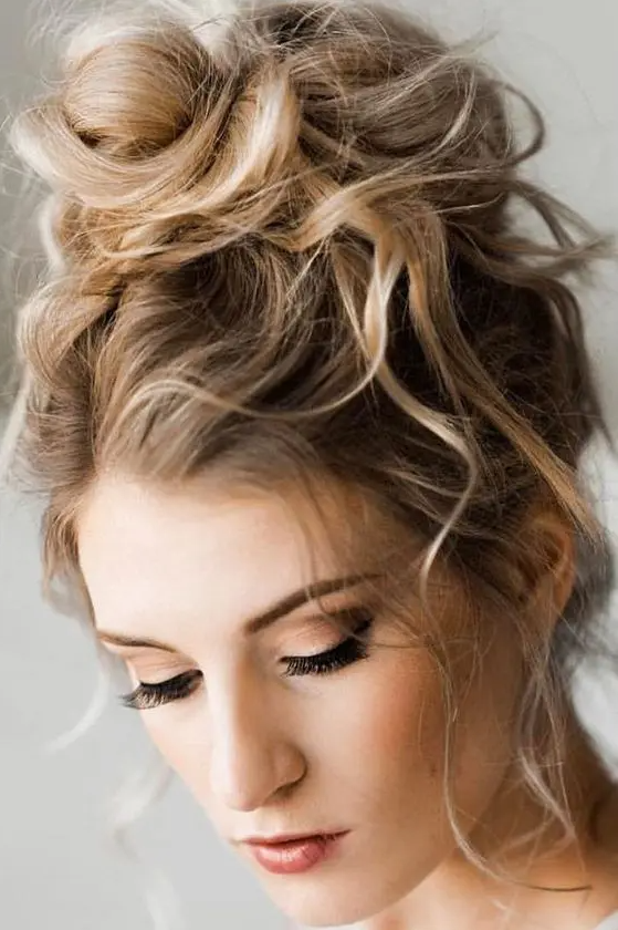a messy and wavy top knot with a wavy top and some locks down is a cool and chic idea with effortless chic