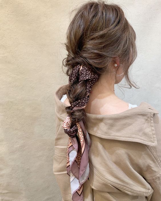 A messy low braid with a messy top and face framing hair plus a printed scarf that is interwoven into the braid