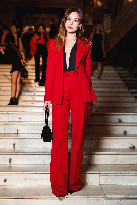 a red power suit with flare pants, black shoes, a black bodysuit with plunging neckline and a small black bag
