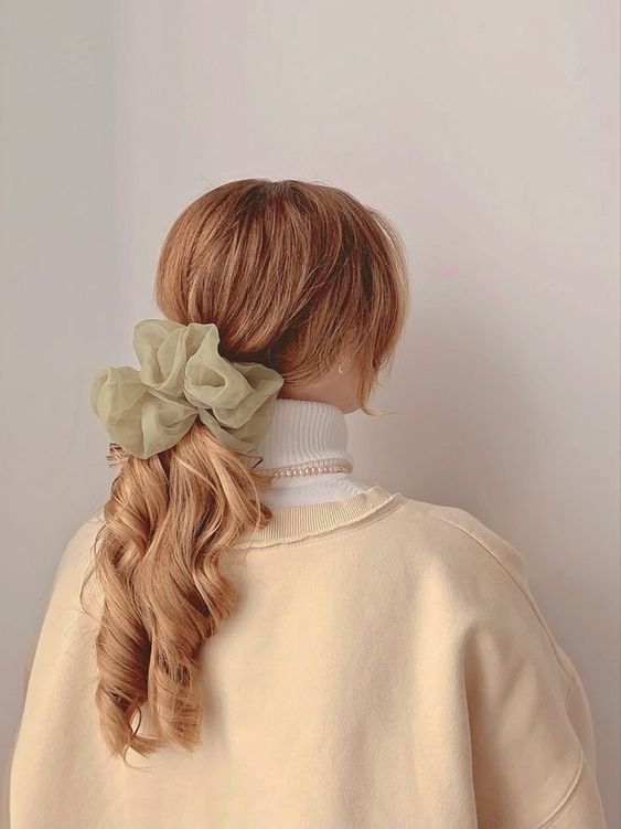 a refined and chic hairstyle of a low curly ponytail and face-framing bangs plus an oversized light green scrunchie