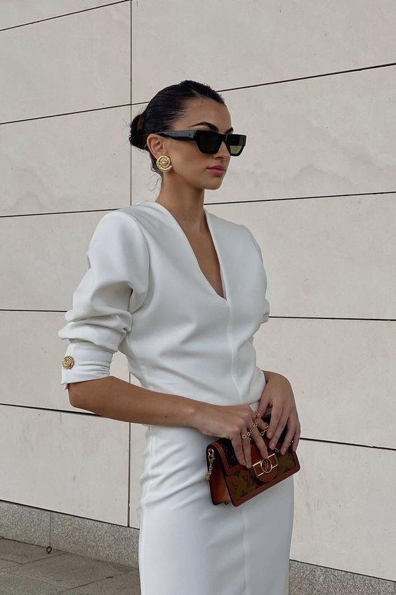 a refined and minimal white plain dress with a V-neckline and short puff sleeves, a small printed bag and statement earrings
