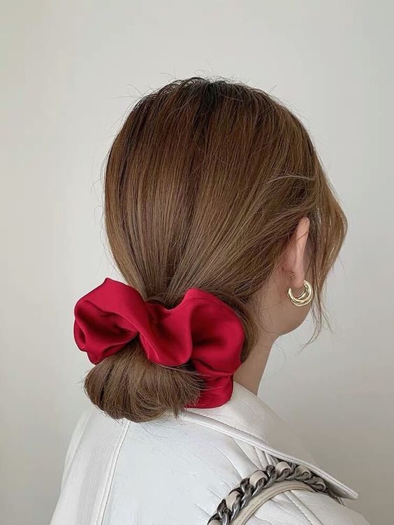 A simple low bun with a volumetric top and face framing plus a large red scrunchie is a cool idea for a Christmas party or some other occasion