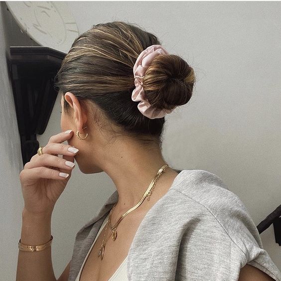 a simple midi bun with a sleek yet volumetric top and a blush scrunchie is a lovely hairstyle to try