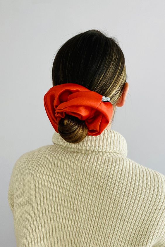a sleek and chic low bun with a sleek top and an oversized red scrunchie as a trendy accent in the hair