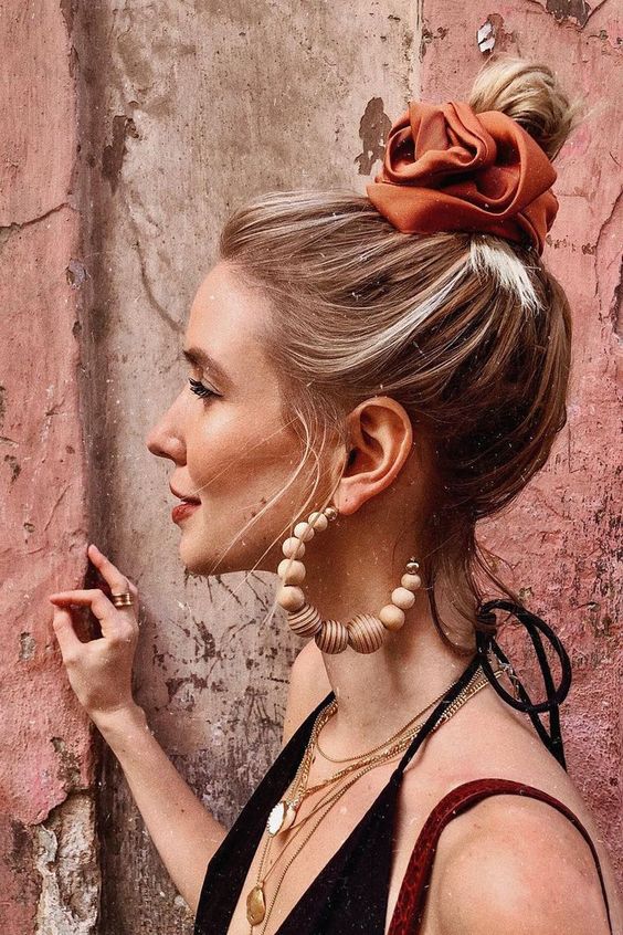 a small messy top knot with a volumetric top and an orange silk scrunchie to secure the bun