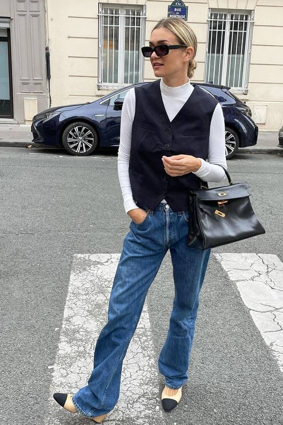 a spring look with a white turtleneck, blue jeans, a black waistcoat, two-tone shoes and a black bag