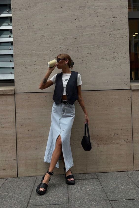 a summer outfit with a white crop top, a black waistcoat, a bleached denim midi, black snadals and a black bag