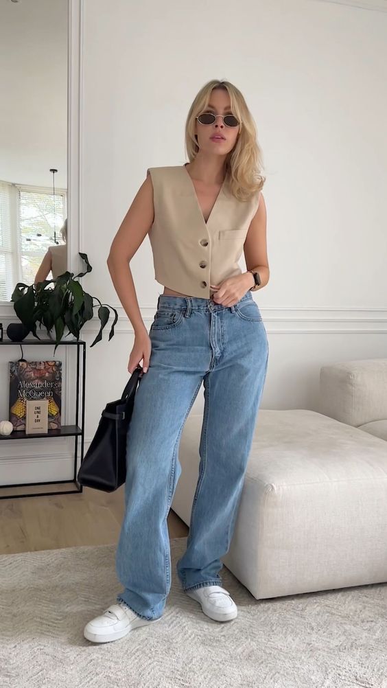 a tan cropped vest, blue jeans, white sneakers and a black bag are a cool and out of the box look for every day