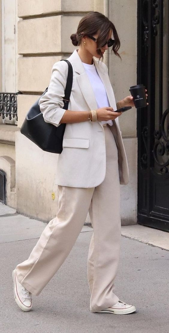 a tan pantsuit, a white t-shirt, white sneakees and a black bag are a cool combo that can be worn to work in spring