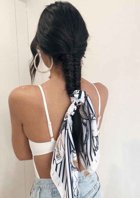 A tight fishtail braid with a volumetric top, face framing bangs and a printed scarf used as a scrunchie is cool