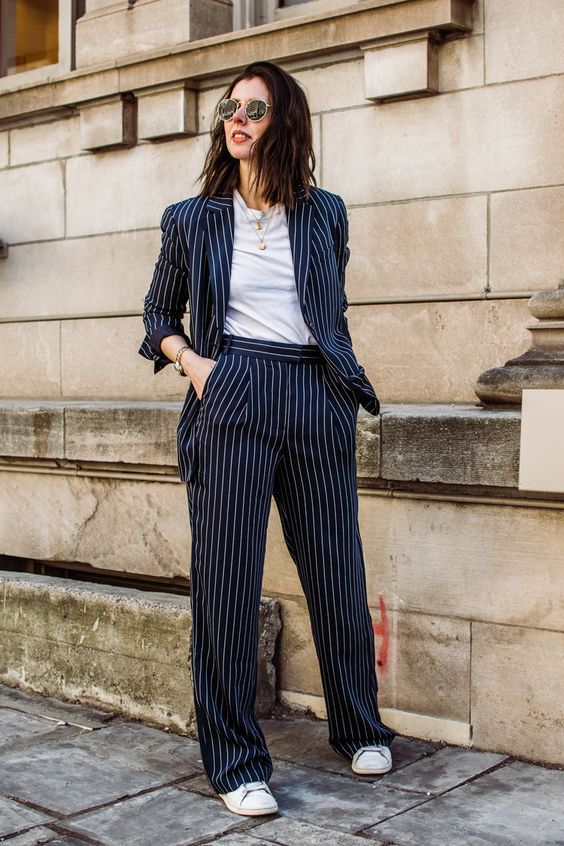 a timeless navy thin stripe pantsuit with a white t-shirt, white sneakers and layered necklaces for a bold look
