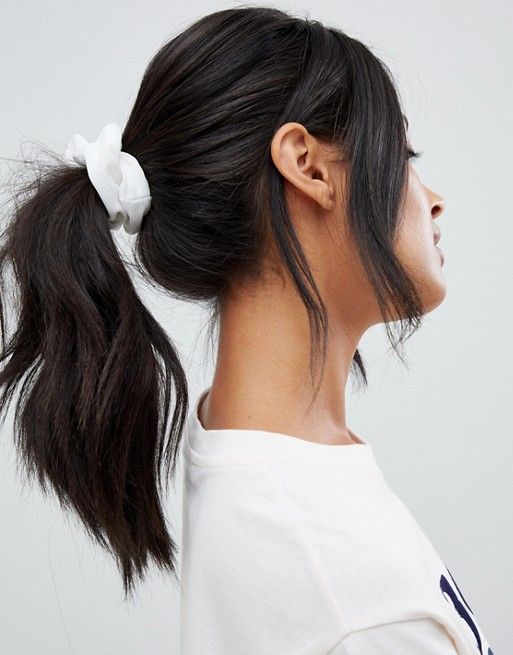 A wavy midi ponytail with a volume on top, face framing bangs and a white scrunchie is a lovely hairstyle