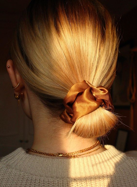 a wrapped low bun with a volumetric top and a caramel silk scrunchie is a cool and casual hairstyle to make