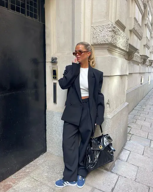 an oversized black pantsuit, a white cro top, blue Adidas sneakers, a large lacquer black bag for spring