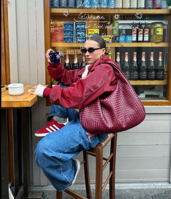 bold blue jeans, a cherry red leather jacket, cherry red sneakers and a large cherry red hobo bag