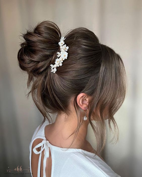 A beautiful messy top knot with a volume on top and face framing hair plus a floral hair piece is a chic idea for a wedding