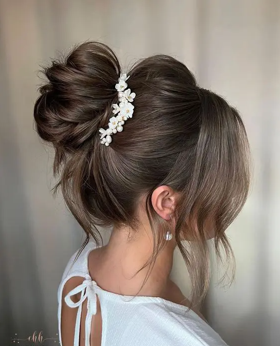 A beautiful messy top knot with a volume on top and face framing hair plus a floral hair piece is a chic idea for a wedding