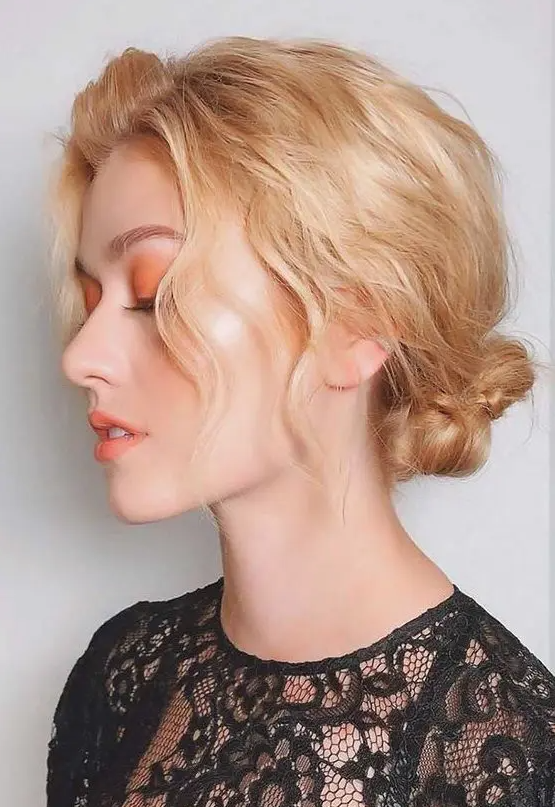 A beautiful wavy braided low bun with a wavy top and some face frmaing hair is a catchy and cool solution for a wedding or a party