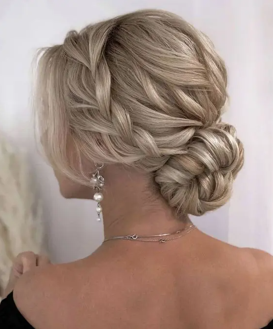 A blonde low bun with a braided halo and a braided top, face framing locks is a chic and stylish idea