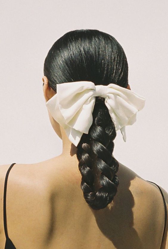 a braid styled as a loop, a sleek top and a large white bow to give a more girlish look to the hairstyle