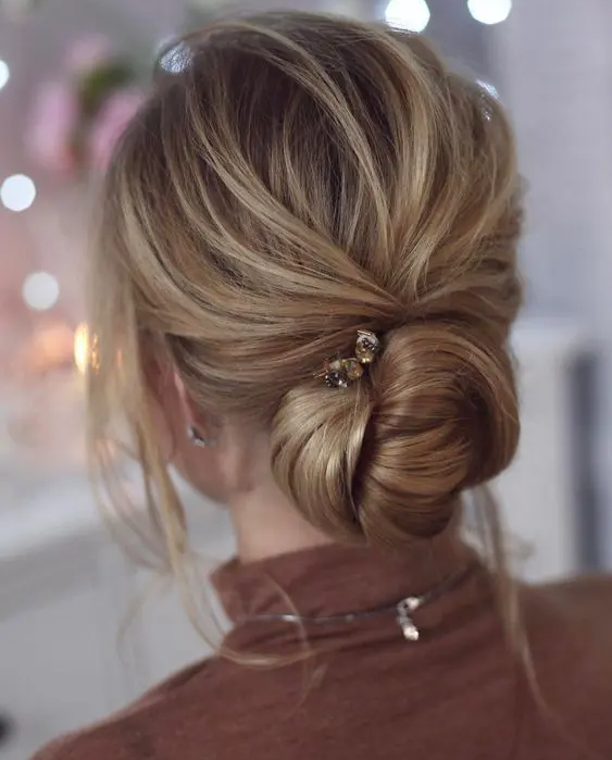 a chic twisted low chignon wedding hairstyle with a bump, locks down and a rhinestone hairpin