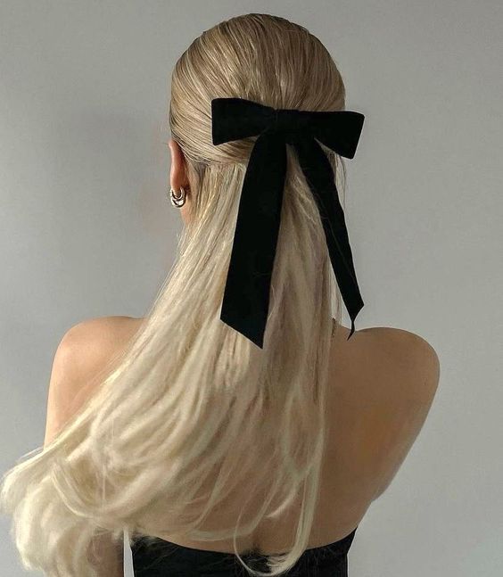a classic half updo with a sleek top and hair down plus a black velvet bow to add a chic and refined touch to the look